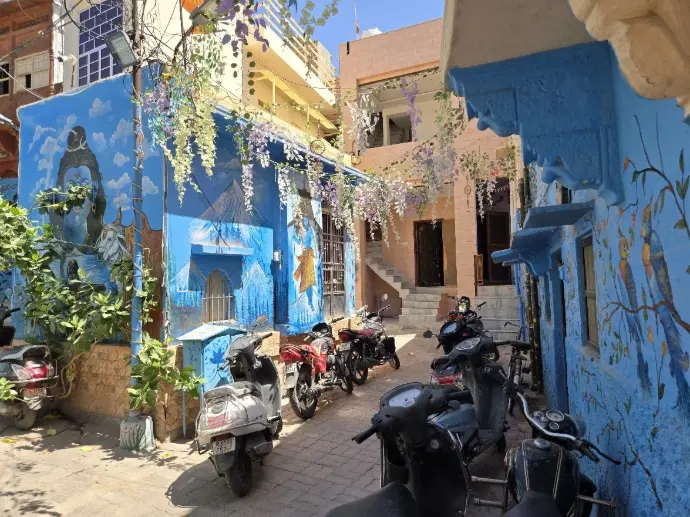 Jour 10 – Jodhpur, entre forteresse et cité bleue La journée est consacrée à la découverte de Jodhpur, surnommée la ville bleue. Dominant la cité depuis son promontoire rocheux, le Fort de Mehrangarh s’impose comme l’une des plus majestueuses forteresses du Rajasthan. Vous en franchissez les lourdes portes et découvrez ses palais intérieurs somptueusement décorés : salles d’audience ornées de fresques, appartements royaux et le célèbre Palais des Miroirs, éclatant de verre coloré et de dorures. Depuis les remparts, la vue plongeante sur la vieille ville bleue est à couper le souffle. La visite se poursuit au Jaswant Thada, élégant cénotaphe en marbre blanc érigé en mémoire du maharaja Jaswant Singh II. Niché au cœur de jardins paisibles, ce lieu empreint de sérénité contraste avec l’animation de la ville. Après un déjeuner dans un restaurant soigneusement sélectionné, vous partez explorer les ruelles pittoresques de la vieille ville. Maisons peintes d’indigo, échoppes débordant de textiles et d’épices, artisans au travail : une immersion authentique dans le quotidien des habitants de Jodhpur. En soirée, votre chauffeur privé vous conduit sur un rooftop avec vue sur le fort illuminé, où vous savourez des spécialités régionales dans une ambiance romantique. Le spectacle des murailles baignées de lumière dorée conclut cette journée riche en émotions. La Ville Bleue